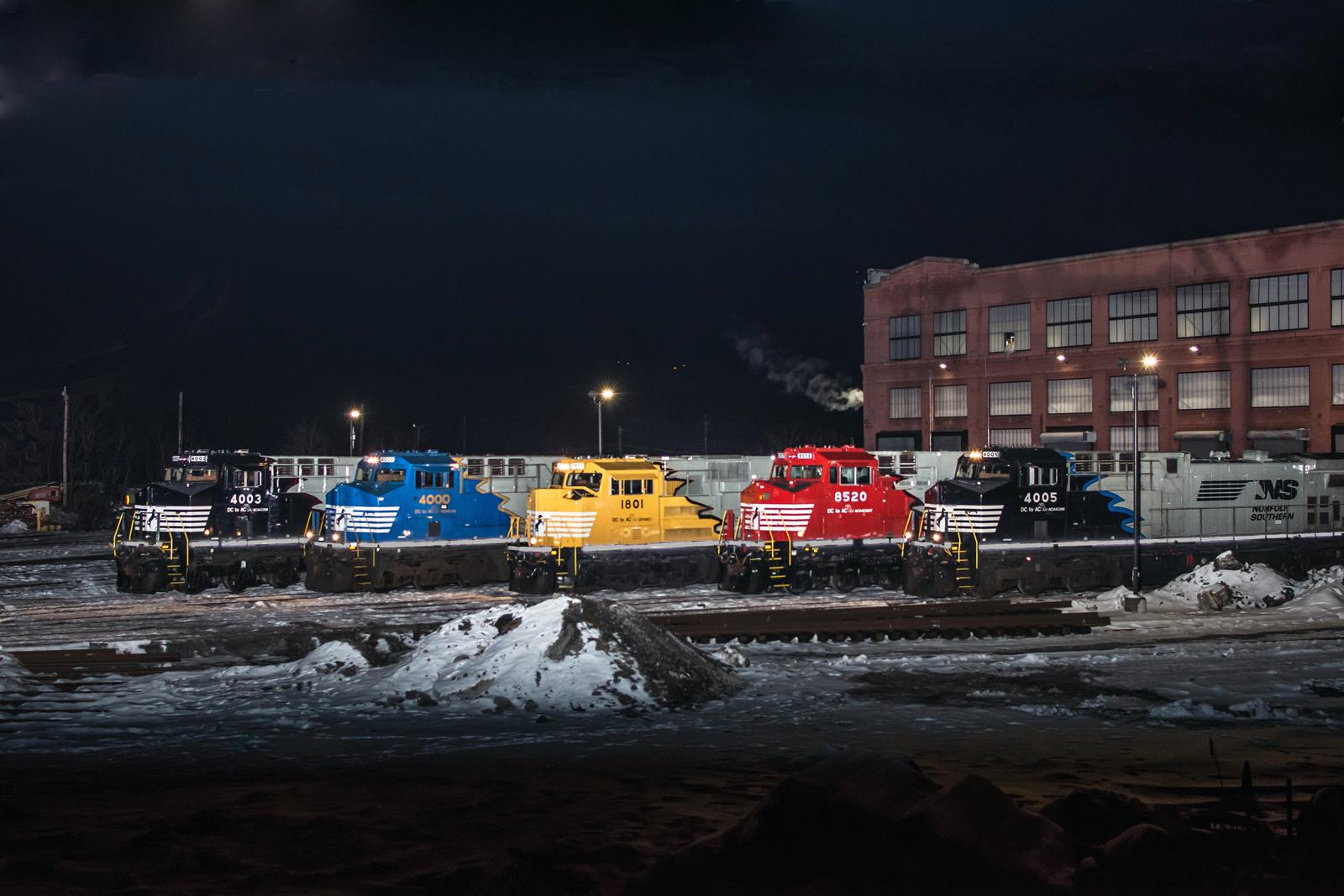 A gathering of five Norfolk Southern DC to AC locomotives sit outside of the Juniata Shops for a company photoshoot. From left to right: 4003 a NS AC44C6M rebuilt in Roanoke featuring a red striping as patronage to the N&W railroad, NS 4000 the AC44C6M rebuilt in Roanoke, NS 1801 a SD70ACC rebuilt by Progess Rail, NS 8520 an AC44C6CF rebuilt by CAF, and NS 4005 a Juniata rebuilt AC44C6M with a blue stripe as patronage to Conrail.  