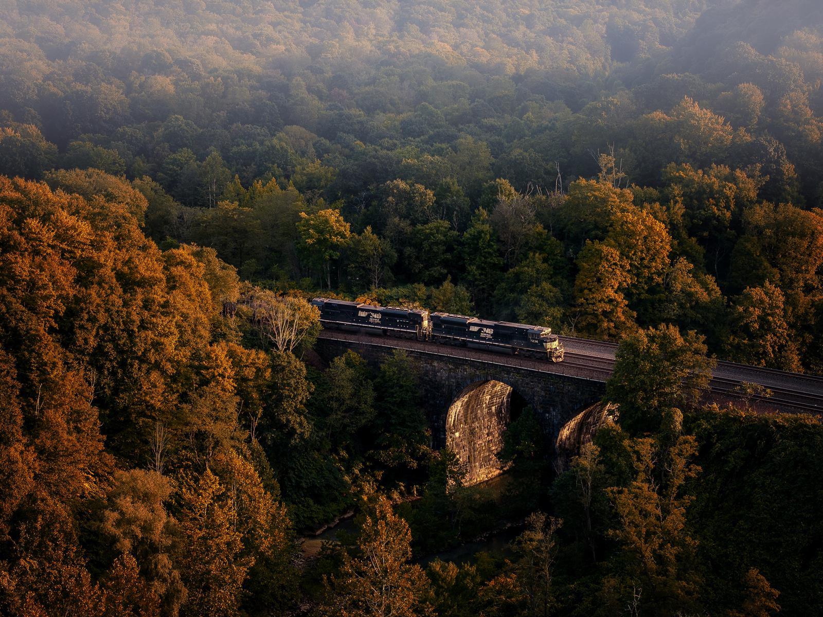 Two Norfolk Southern EMD SD70ACUs shove a n eastbound coal train over "Big Viaduct" in South Fork, crossing the Little Conemaugh River with vibrant fall foliage.